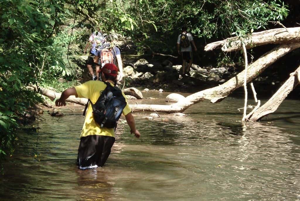 #Pra-todos-verem:o-que-fazer-em-Carrancas-a-imagem-mostra-quatro-rapazes-percorrendo-trilha-num-rio